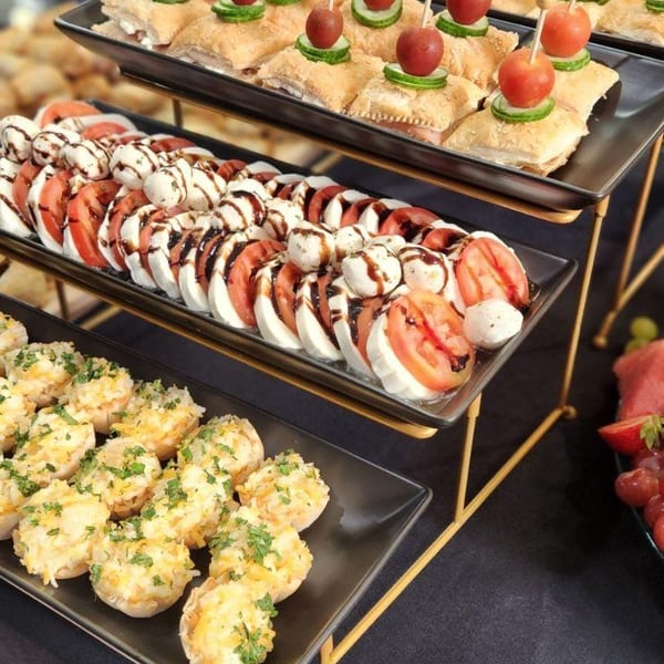 Three tiers of appetizers, including tomato and mozzarella, puff pastry bites, and stuffed mushrooms.