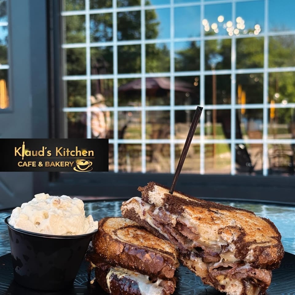 A grilled sandwich with melted cheese and meat, served with a side of potato salad.