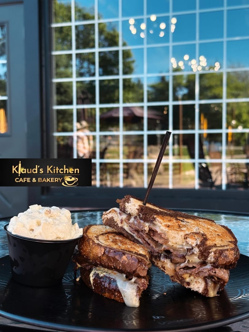 A grilled sandwich with melted cheese and meat, served with a side of potato salad.