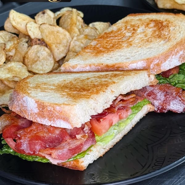 A Klaud's Kitchen BLT sandwich with crispy bacon, lettuce, and tomato, served with potato chips.