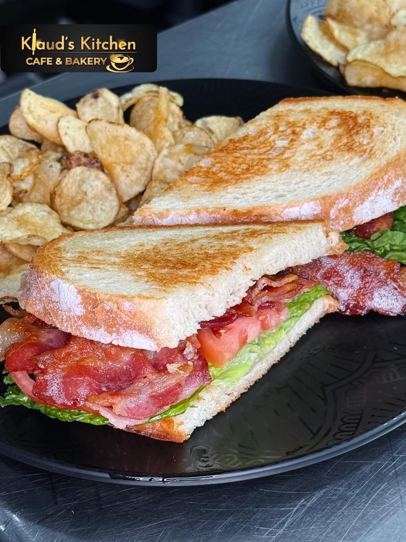 A Klaud's Kitchen BLT sandwich with crispy bacon, lettuce, and tomato, served with potato chips.