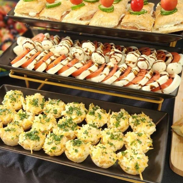 Three tiers of appetizers: mini pastries with cherry tomatoes, caprese skewers, and cheesy tartlets with parsley.