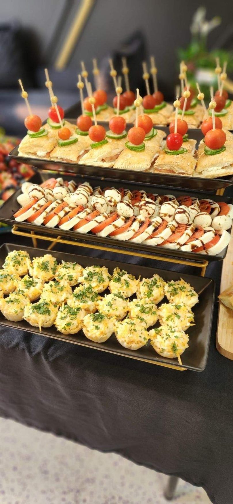 Three tiers of appetizers: mini pastries with cherry tomatoes, caprese skewers, and cheesy tartlets with parsley.