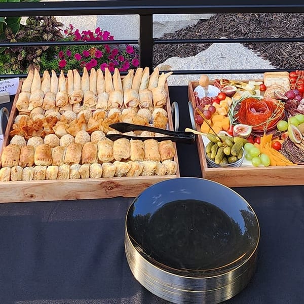 An outdoor buffet table with grapes, pastries, charcuterie, vegetables, and fruit platters.